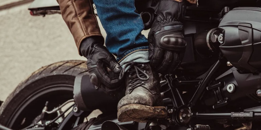 A loose legger wearing purpose-built motorcycle boots folds the cuffs of his jeans to prevent them from getting caught on motorcycle parts while riding.